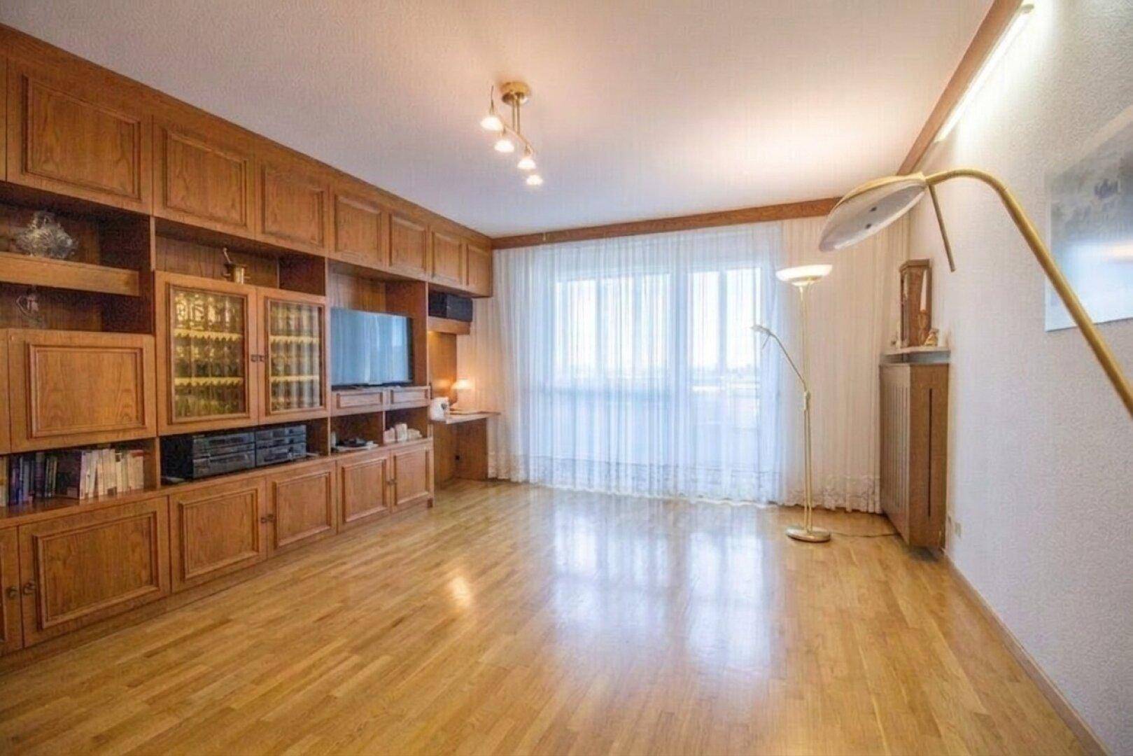 Helles Wohnzimmer mit großer Fensterfront, Holzboden und integrierter Schrankwand.
