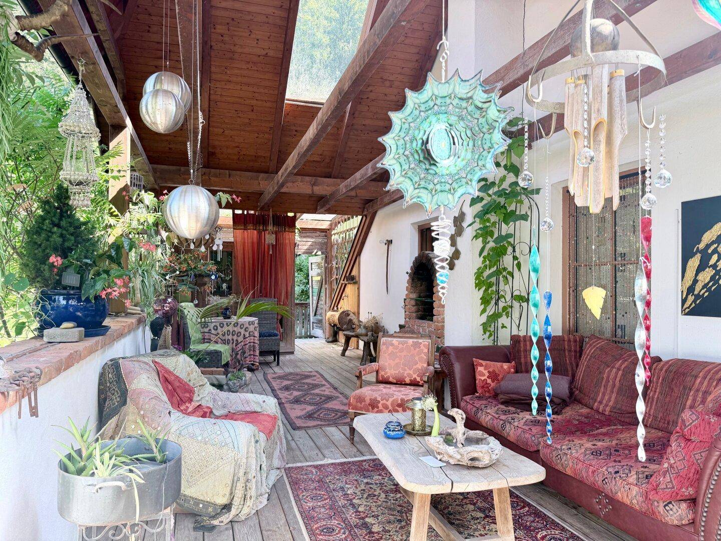 Gemütliche überdachte Terrasse mit vielen Pflanzen, bunten Dekorationen und bequemen Sitzgelegenheiten.