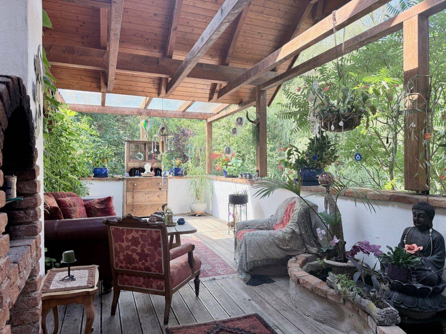Entspannende überdachte Terrasse mit Holzboden, bequemen Möbeln und Blick ins Grüne.