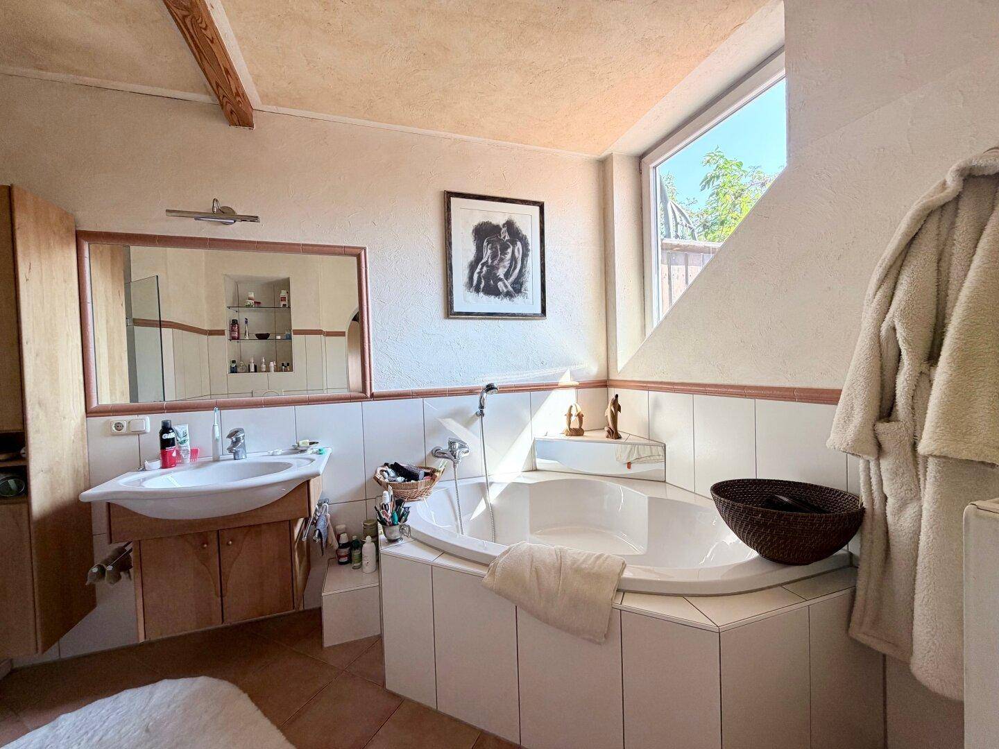 Helles Badezimmer mit Eckbadewanne, Waschtisch und schrägen Decken mit Holzbalken.