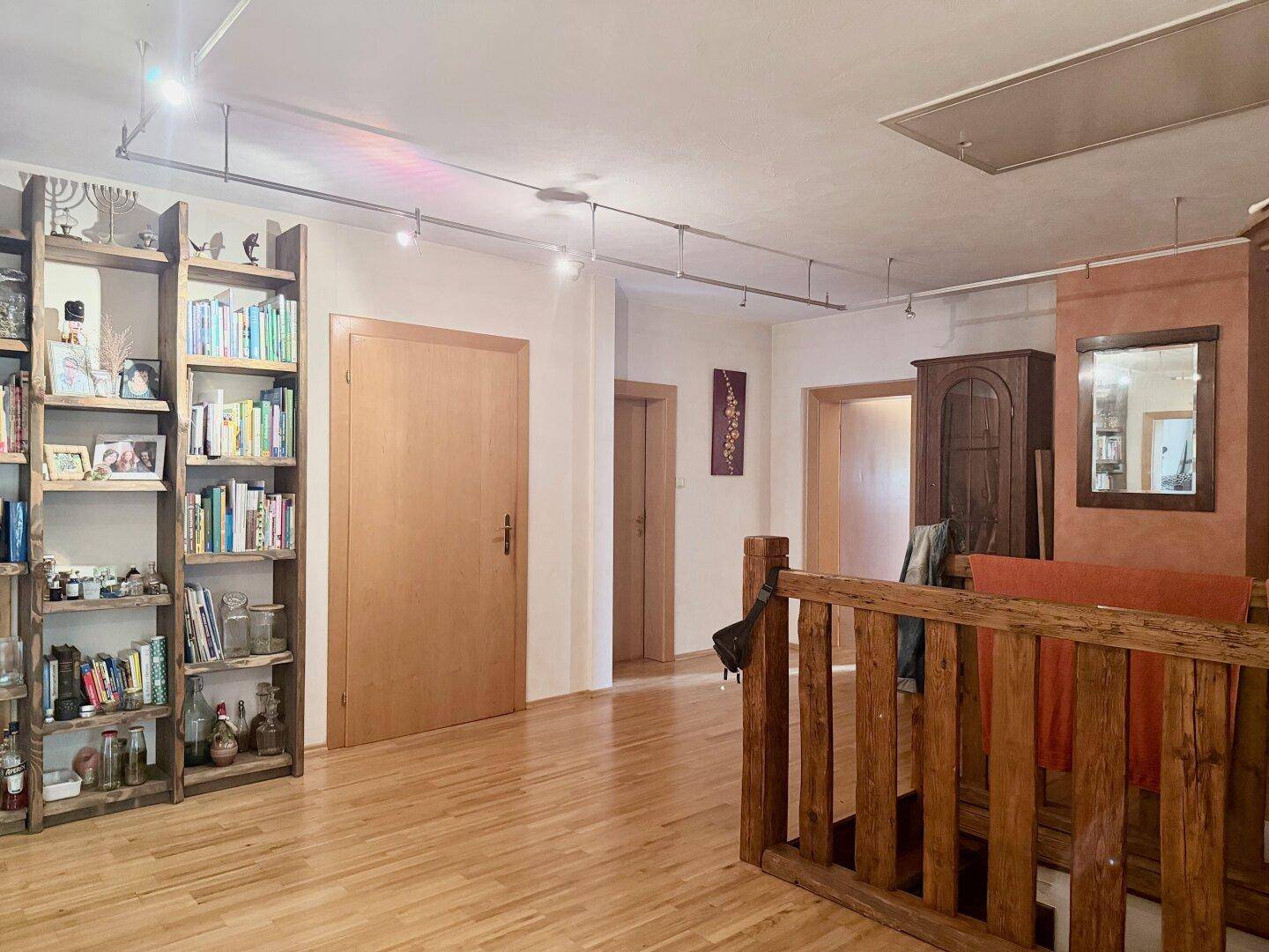 Heller Flur mit Holzboden, Bücherregal und Zugang zu weiteren Räumen.