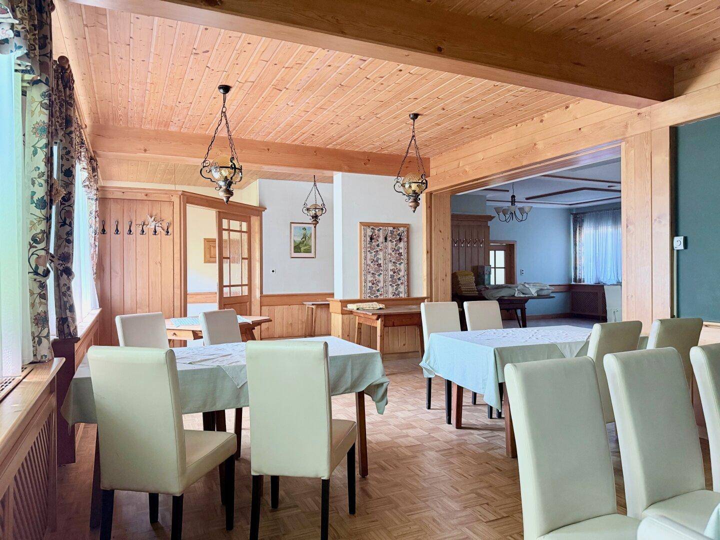 Großer Speisesaal mit Holzbalken, hellen Tischen und Stühlen für Veranstaltungen.
