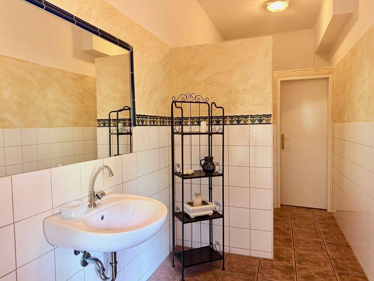 Badezimmer mit Waschbecken, großem Spiegel und traditionellen Fliesen an Wänden und Boden.
