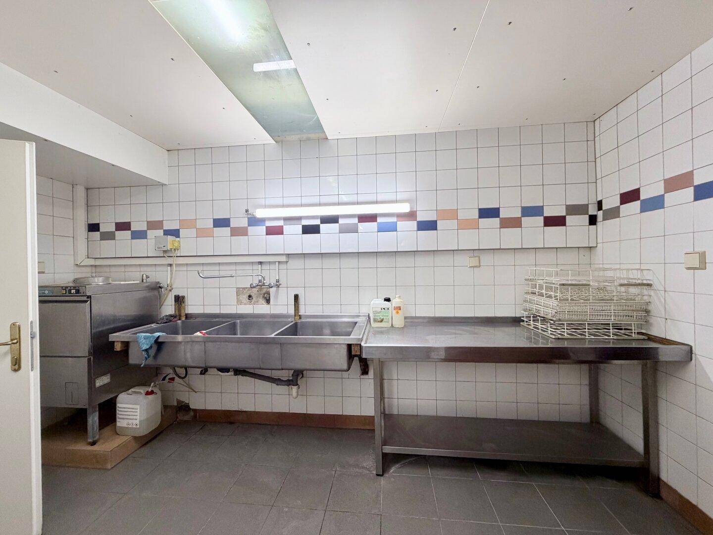 Gewerbliche Küche mit großen Edelstahlspülen, Spülmaschine und gefliesten Wänden.