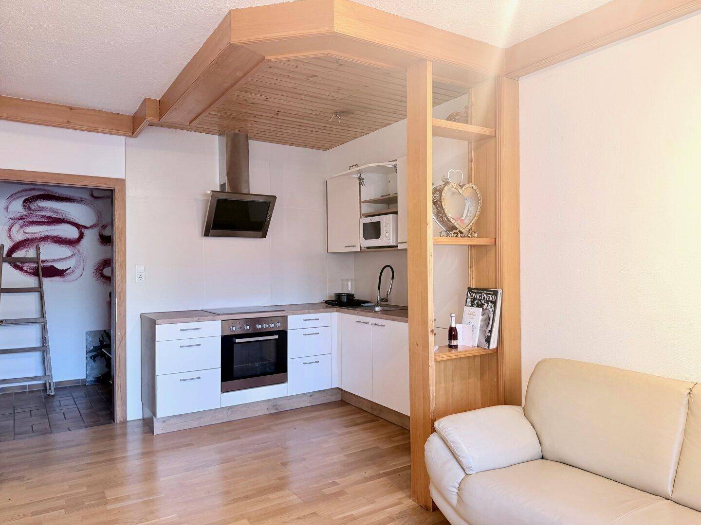 Heller Wohnbereich mit kleiner Küchenzeile, Holzbalkendecke und gemütlichem Sofa.