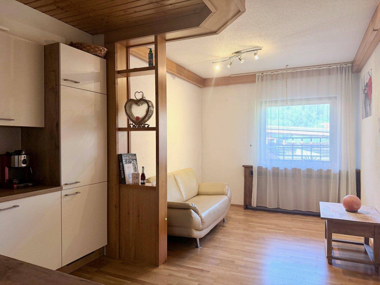 Gemütlicher Wohnbereich mit integrierter Küchenzeile und Fenster, das viel Tageslicht hereinlässt.