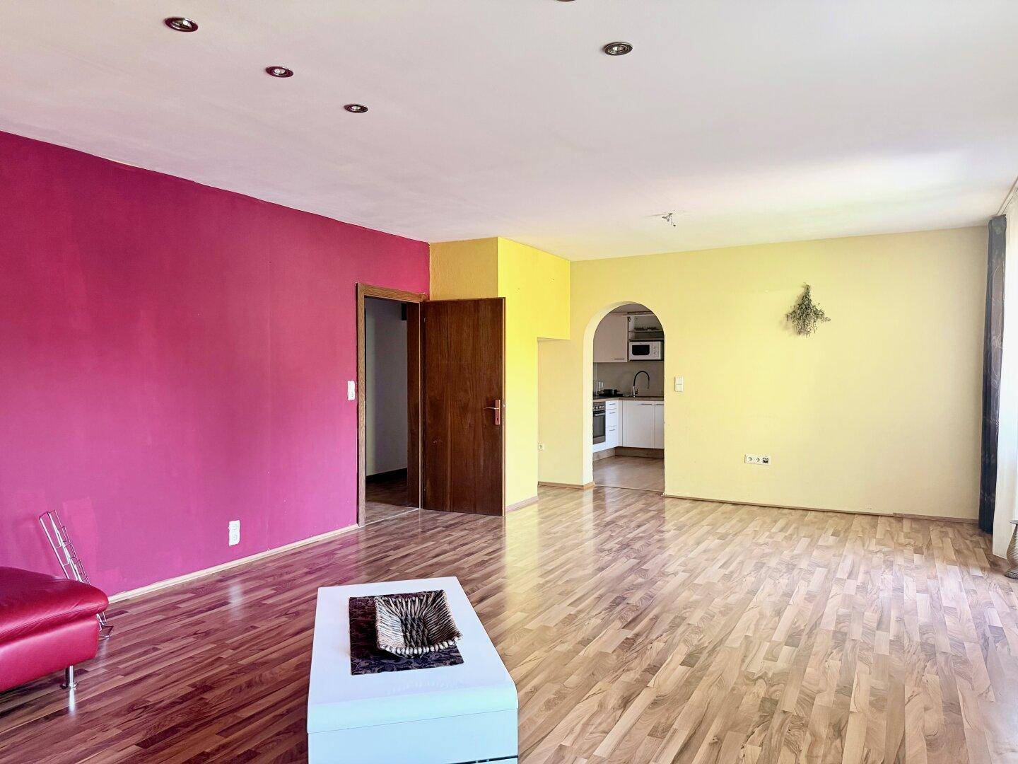 Geräumiges Wohnzimmer mit farbenfrohen Wänden, Laminatboden und Durchgang zu einem weiteren Raum.