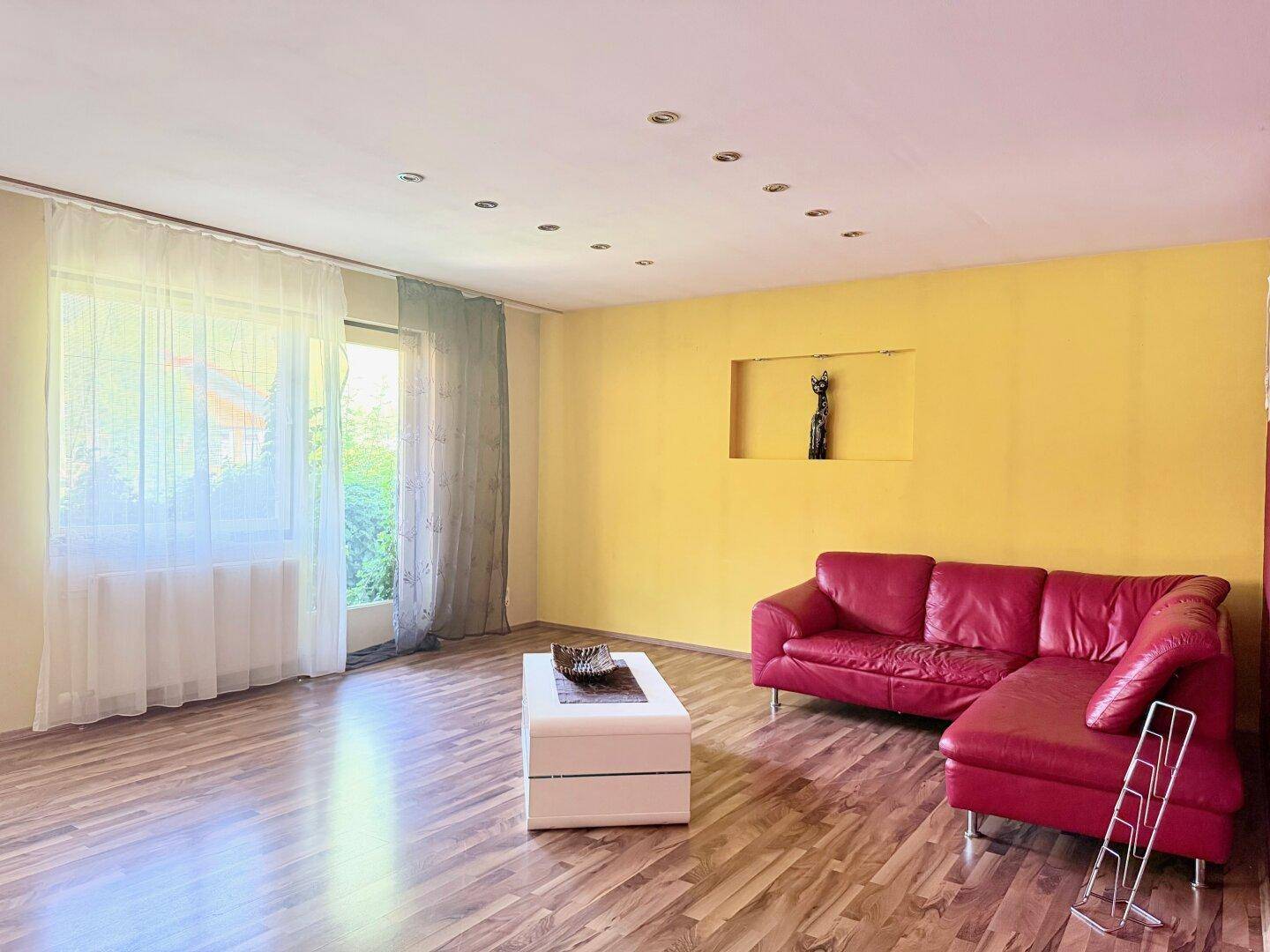 Helles Wohnzimmer mit lebhaften Wänden, rotem Sofa und großem Fenster für viel Tageslicht.