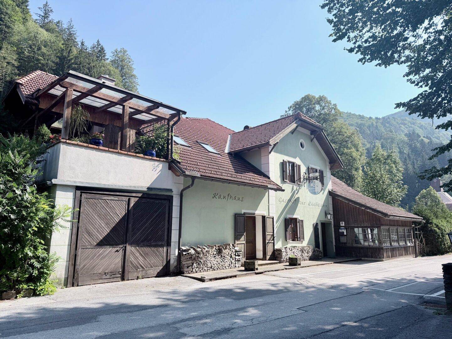 Historisches Gasthaus mit traditioneller Architektur, umgeben von üppiger Natur und Bergen.