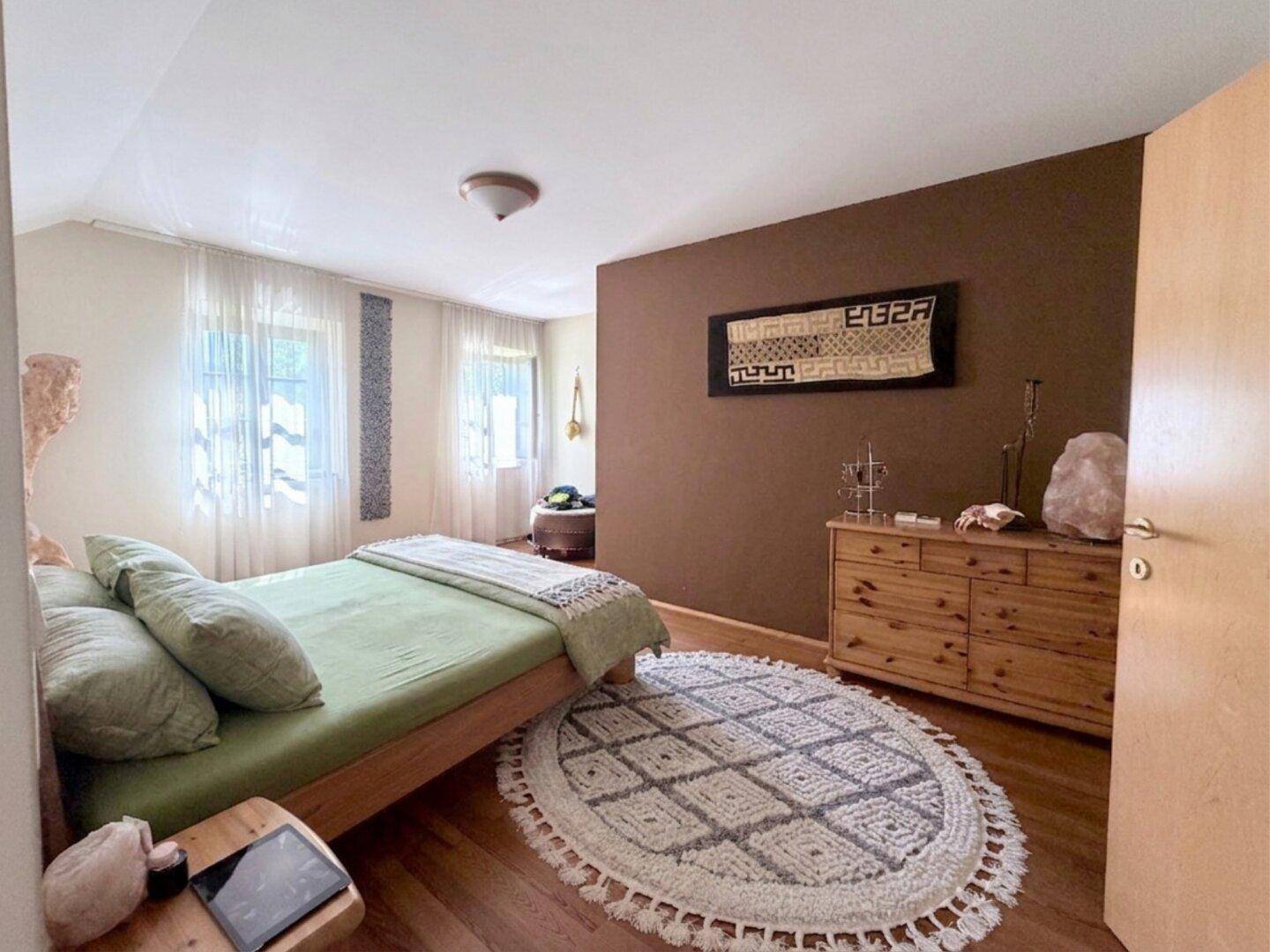 Gemütliches Schlafzimmer mit Holzboden, brauner Akzentwand und natürlichem Licht.