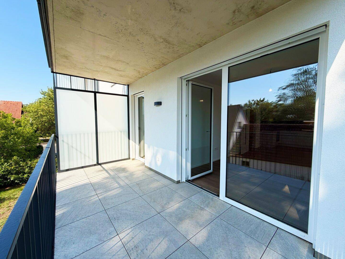 Heller Balkon mit Schiebetüren zum Innenraum und moderner Verglasung für Privatsphäre.