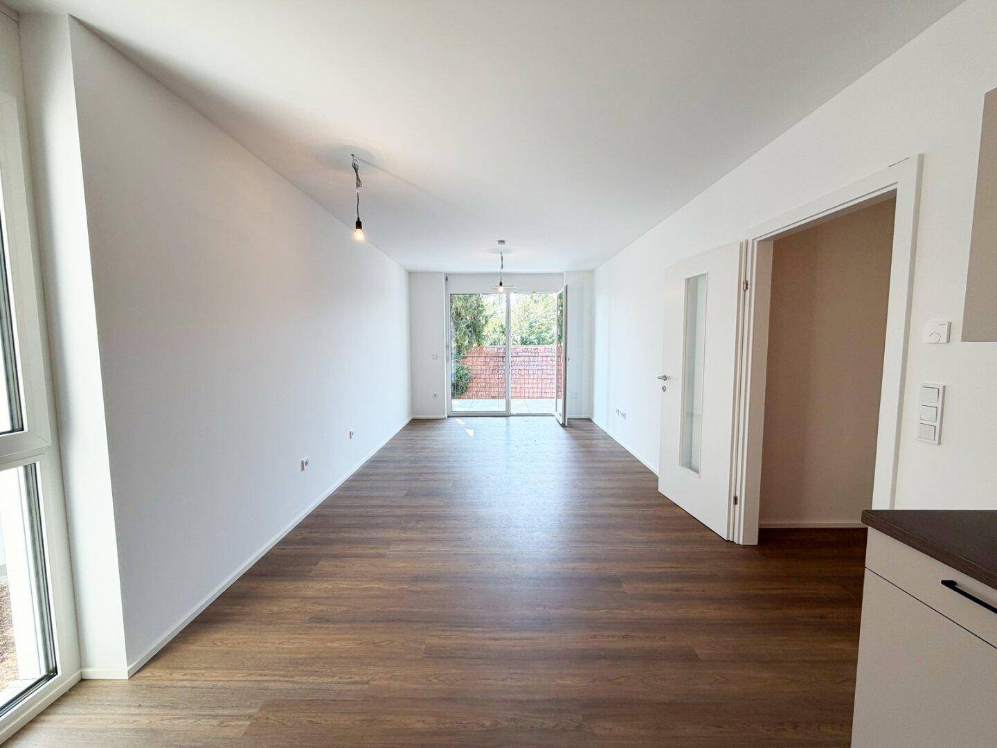 Langer, heller Wohnbereich mit Laminatboden und Zugang zu einem Außenbereich, ideal für gemütliche Abende.
