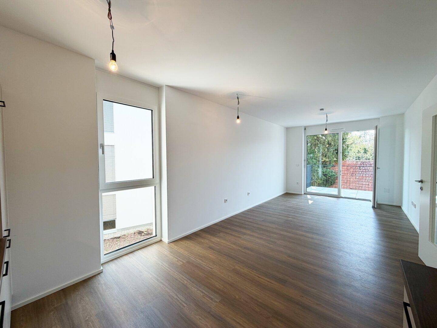 Lichtdurchfluteter Wohnraum mit großen Fenstern und Zugang zum Balkon, bietet viel Tageslicht.