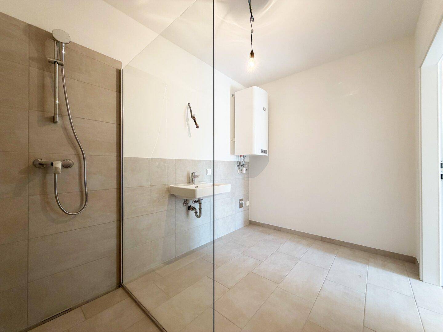 Modernes Badezimmer mit großer Glasdusche und Waschbecken, bietet viel Platz und Helligkeit.