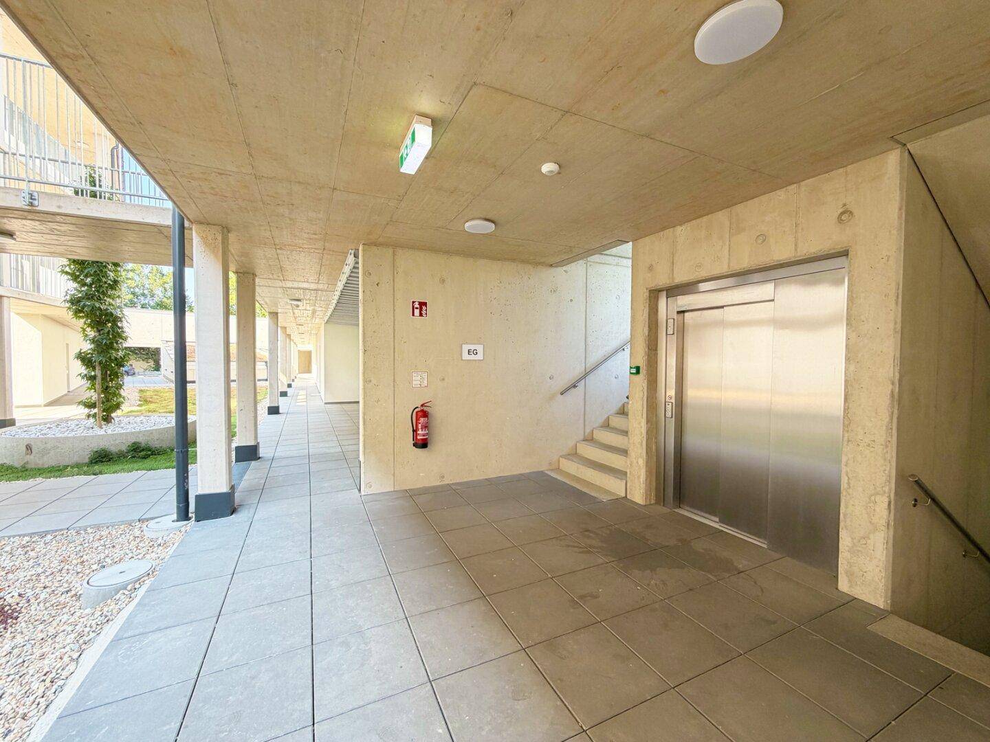 Moderner Eingangsbereich des Gebäudes mit Aufzug und Treppenhaus, barrierefrei zugänglich.