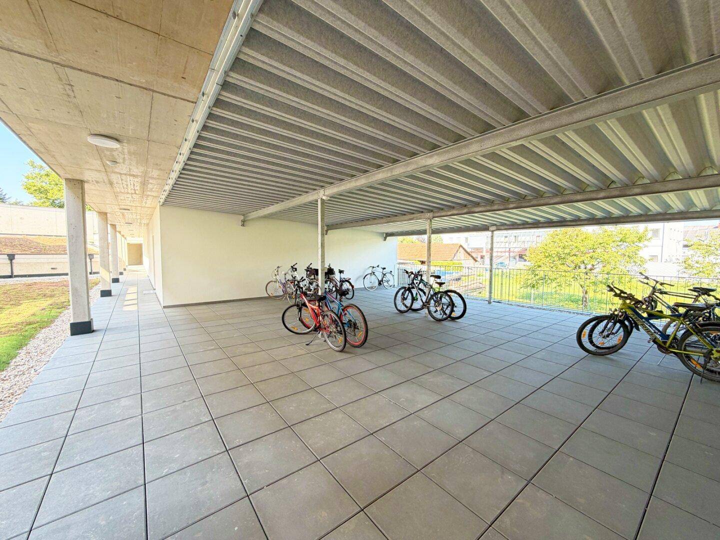Überdachter Fahrradabstellplatz mit Fliesenboden, bietet sicheren Schutz für Fahrräder.