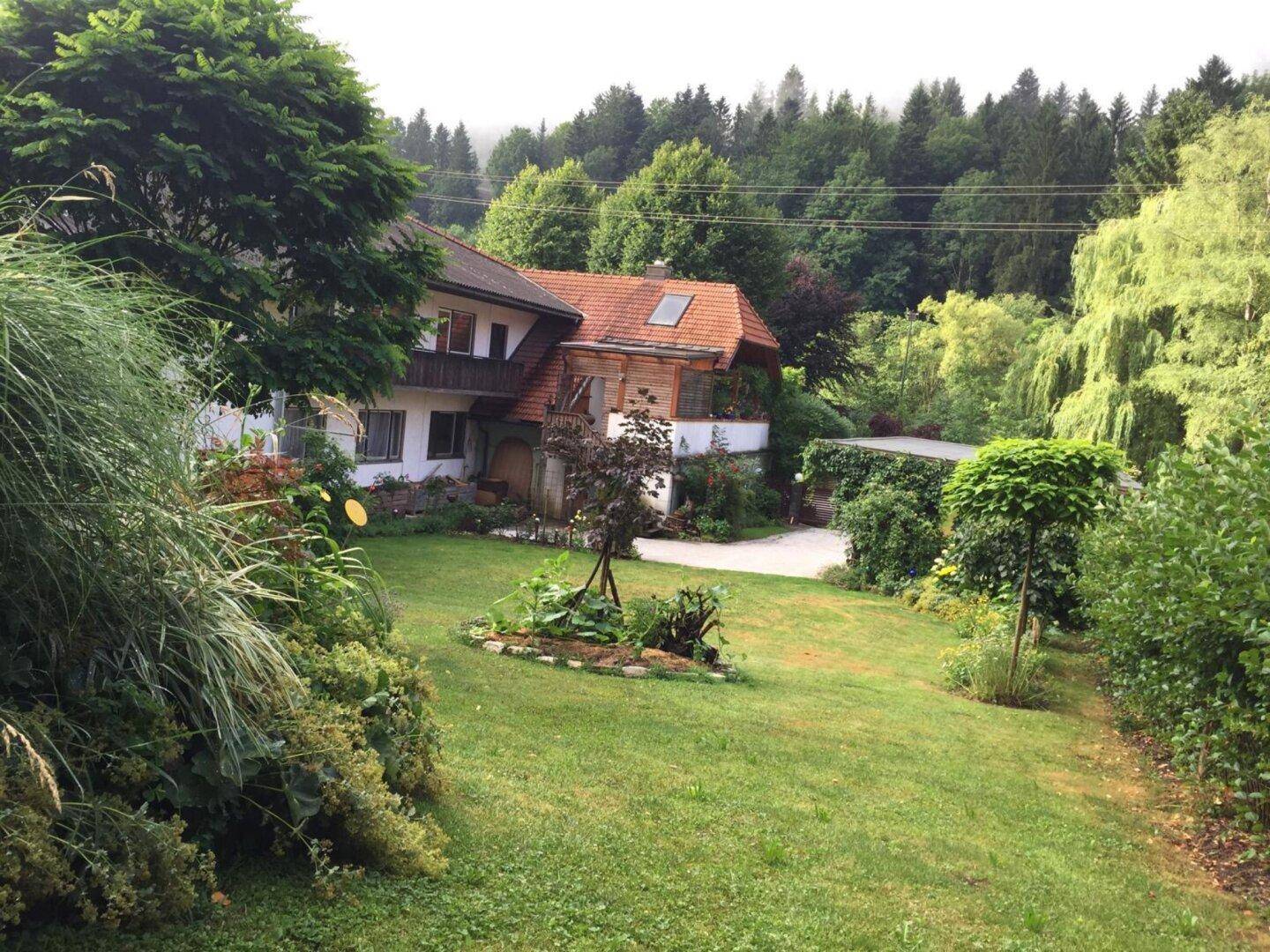 Charmantes Haus mit großem, gepflegtem Garten, umgeben von üppiger Natur und Bäumen.