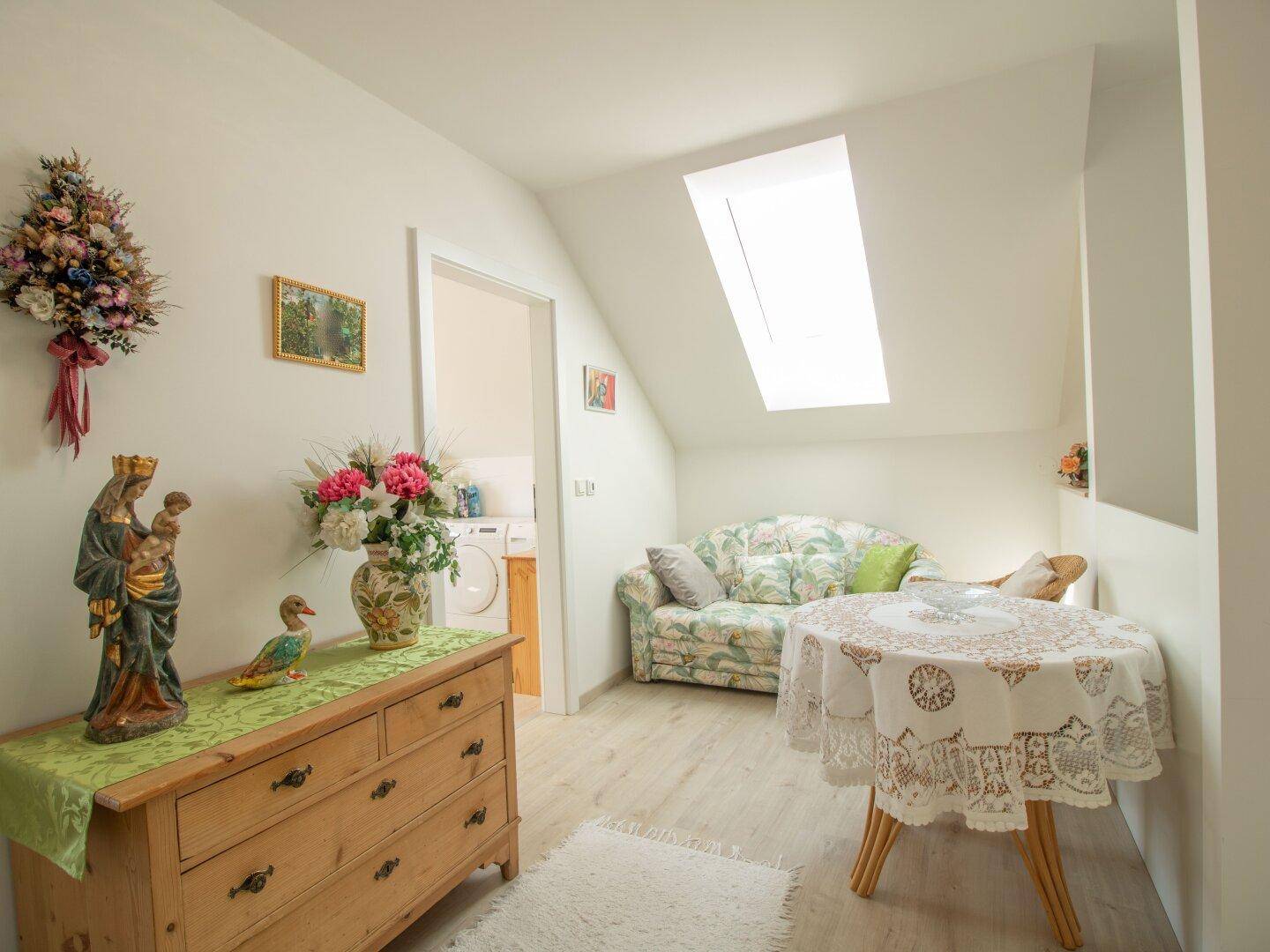 Gemütlicher Wohnbereich im Dachgeschoss mit Sofa, Tisch und natürlichem Licht durch ein Dachfenster.