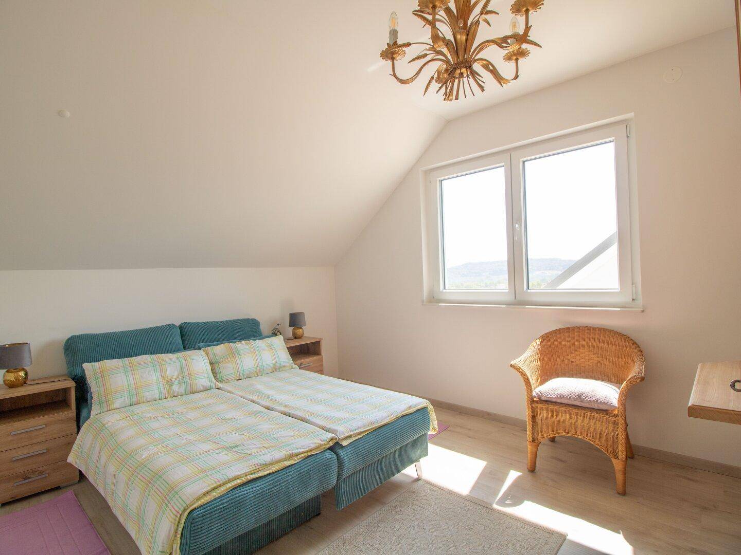 Helles Schlafzimmer im Dachgeschoss mit Doppelbett, Dachschräge und weitem Ausblick durch das Fenster.