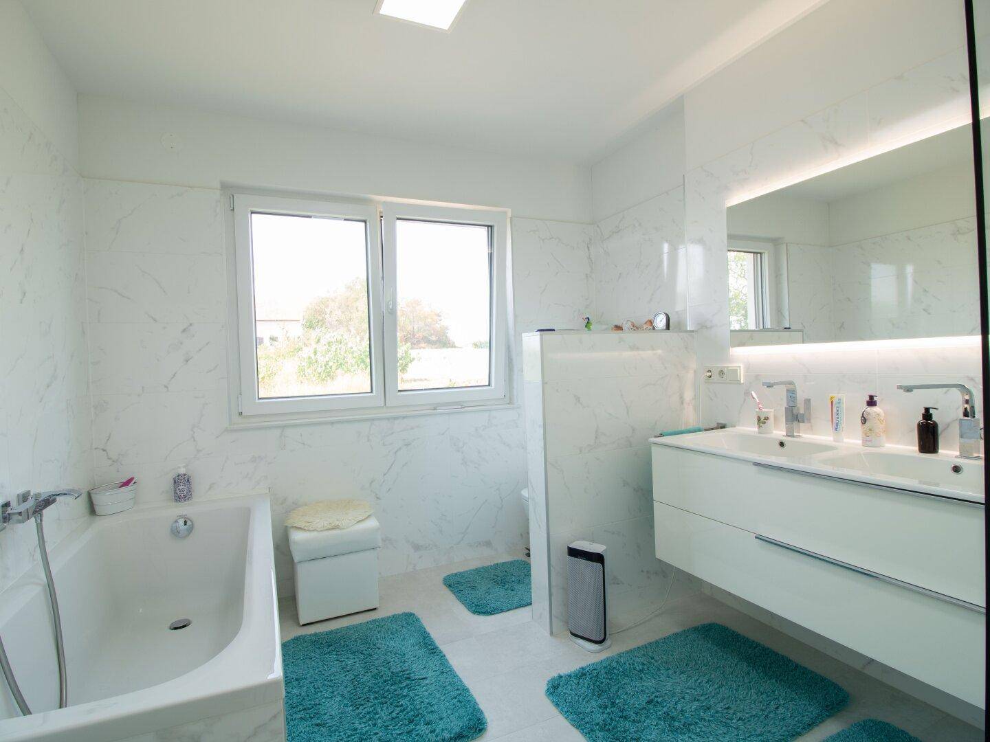 Modernes Badezimmer mit Badewanne, Doppelwaschbecken und großem Fenster für viel Tageslicht.