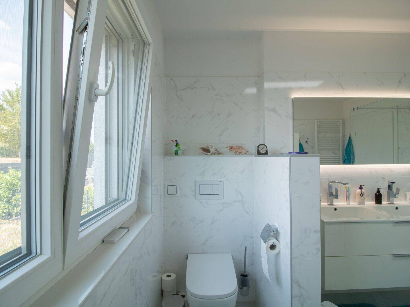 Helles Badezimmer mit WC, Fenster und modernen Fliesen in Marmoroptik.
