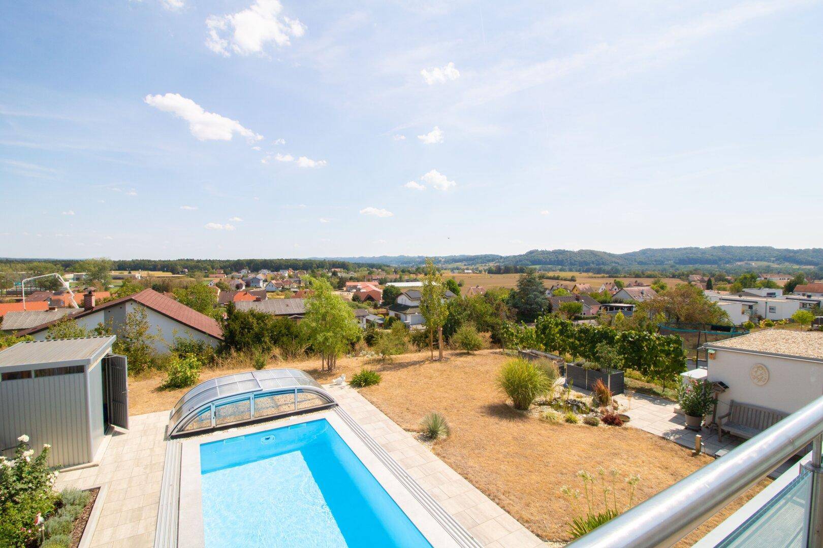 Blick vom Balkon auf den Pool, den Garten und die malerische Landschaft in der Ferne.