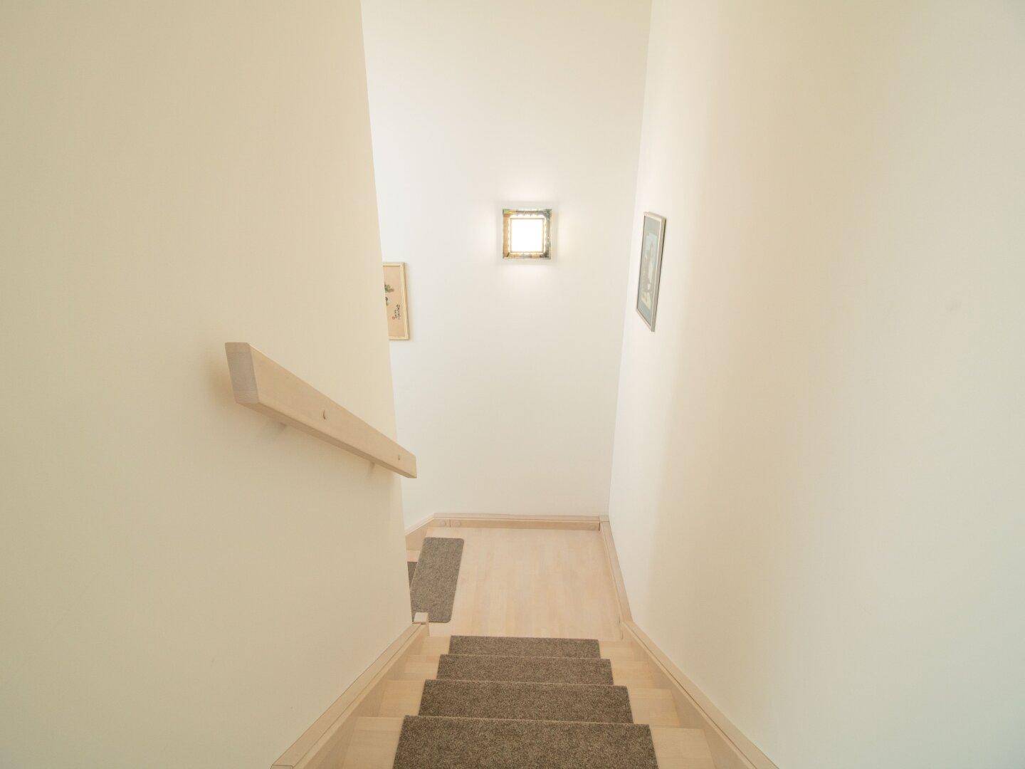 Heller Treppenaufgang mit Teppichstufen und Holzgeländer, der in die untere Etage führt.