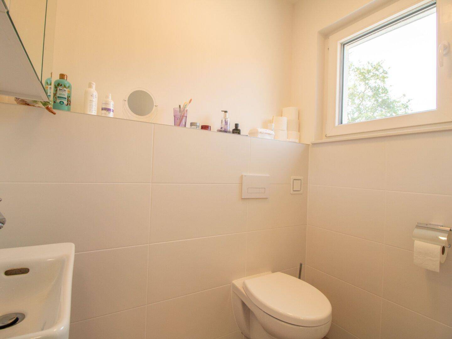 Helles Gäste-WC mit Fenster, weiß gefliesten Wänden und kleinem Waschbecken.