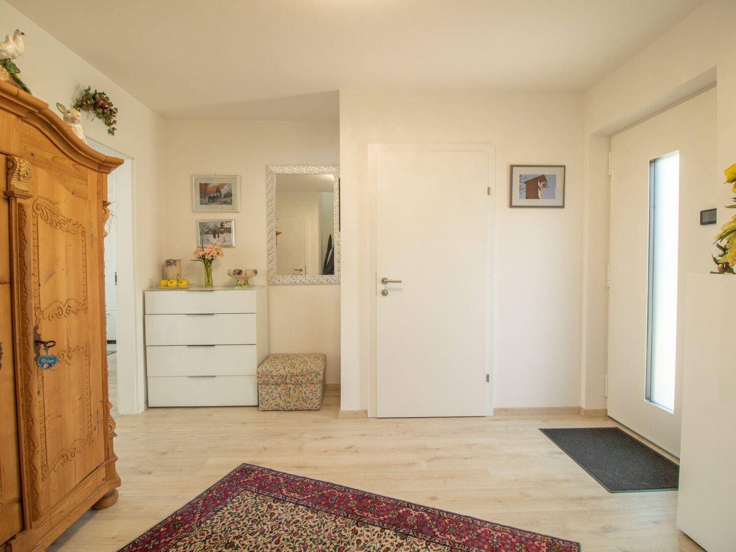 Heller Eingangsbereich mit Holzschrank, Spiegel und moderner Haustür.