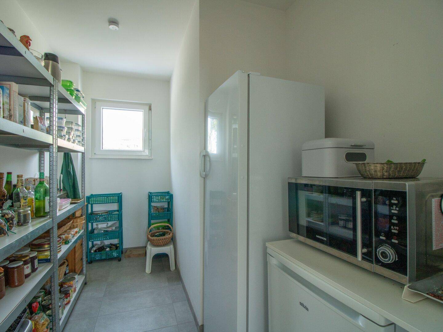 Praktische Speisekammer mit Regalen, Kühlschrank und kleinem Fenster für Belüftung.