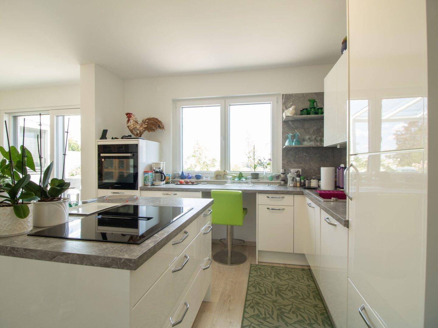 Geräumige Küche mit Kücheninsel, integriertem Backofen und viel Tageslicht durch große Fenster.