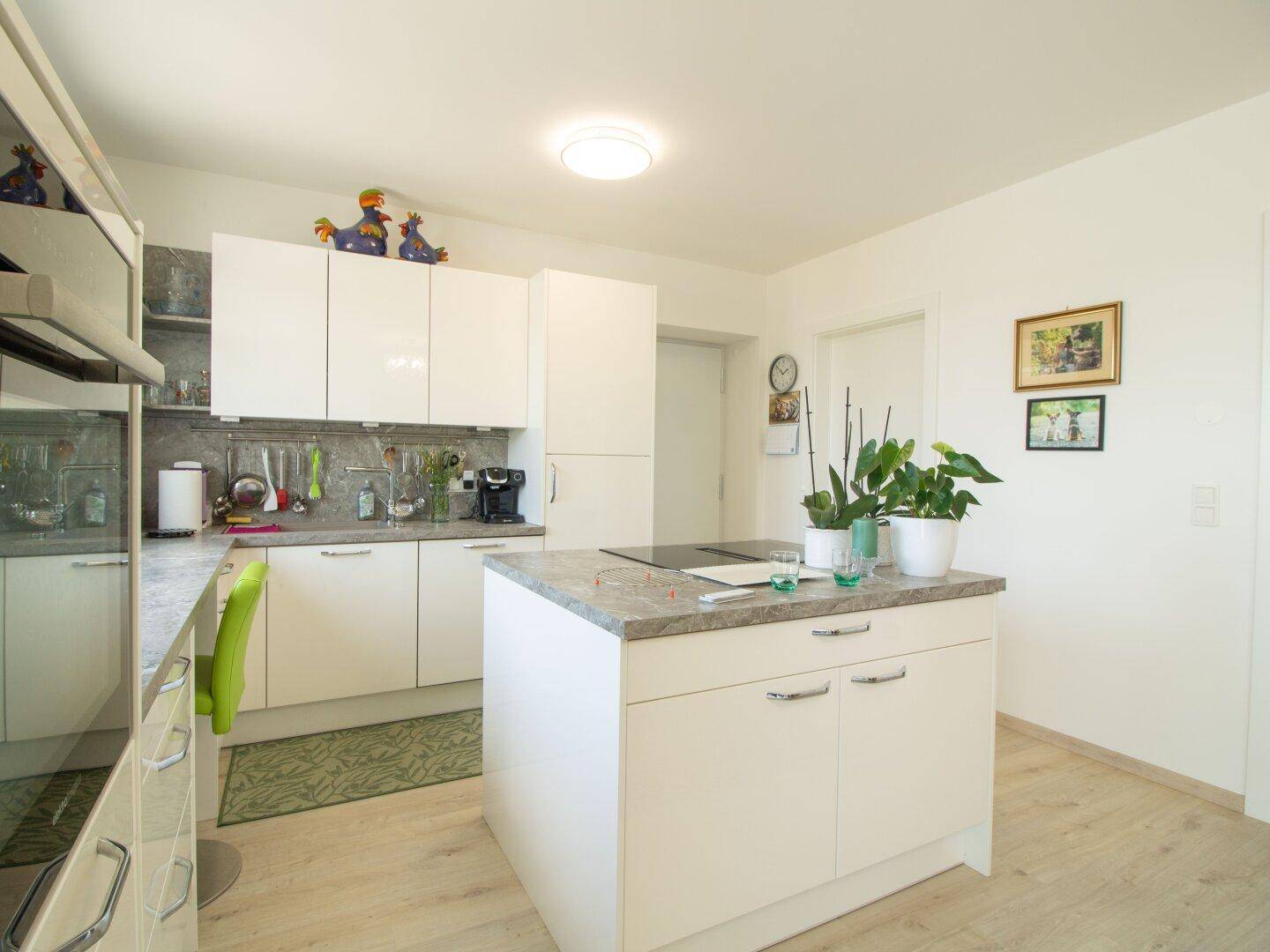 Moderne Küche mit weißer Hochglanzfront, Kücheninsel und hellem Laminatboden.