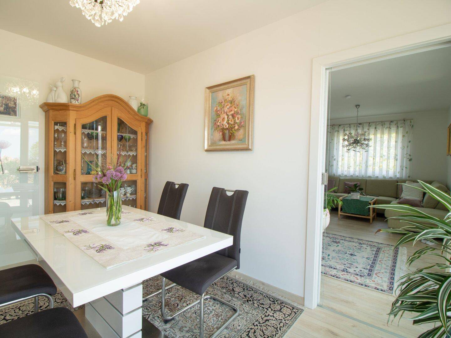 Gemütlicher Essbereich mit Holztisch, Vitrinenschrank und Blick ins angrenzende Wohnzimmer.