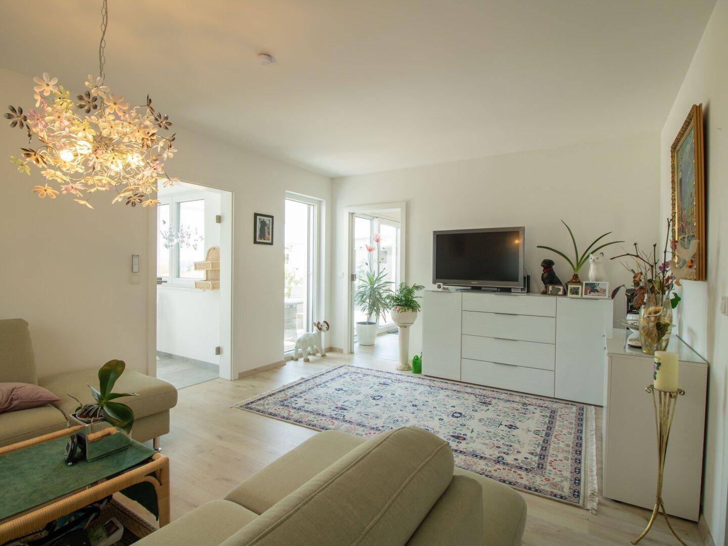 Helles Wohnzimmer mit beigem Sofa, Teppich und Zugang zu einem Außenbereich.