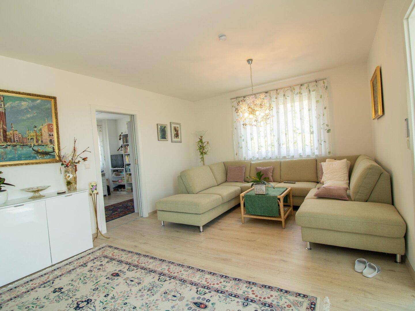 Geräumiges Wohnzimmer mit Ecksofa, Teppich und Blick auf den Garten durch das Fenster.