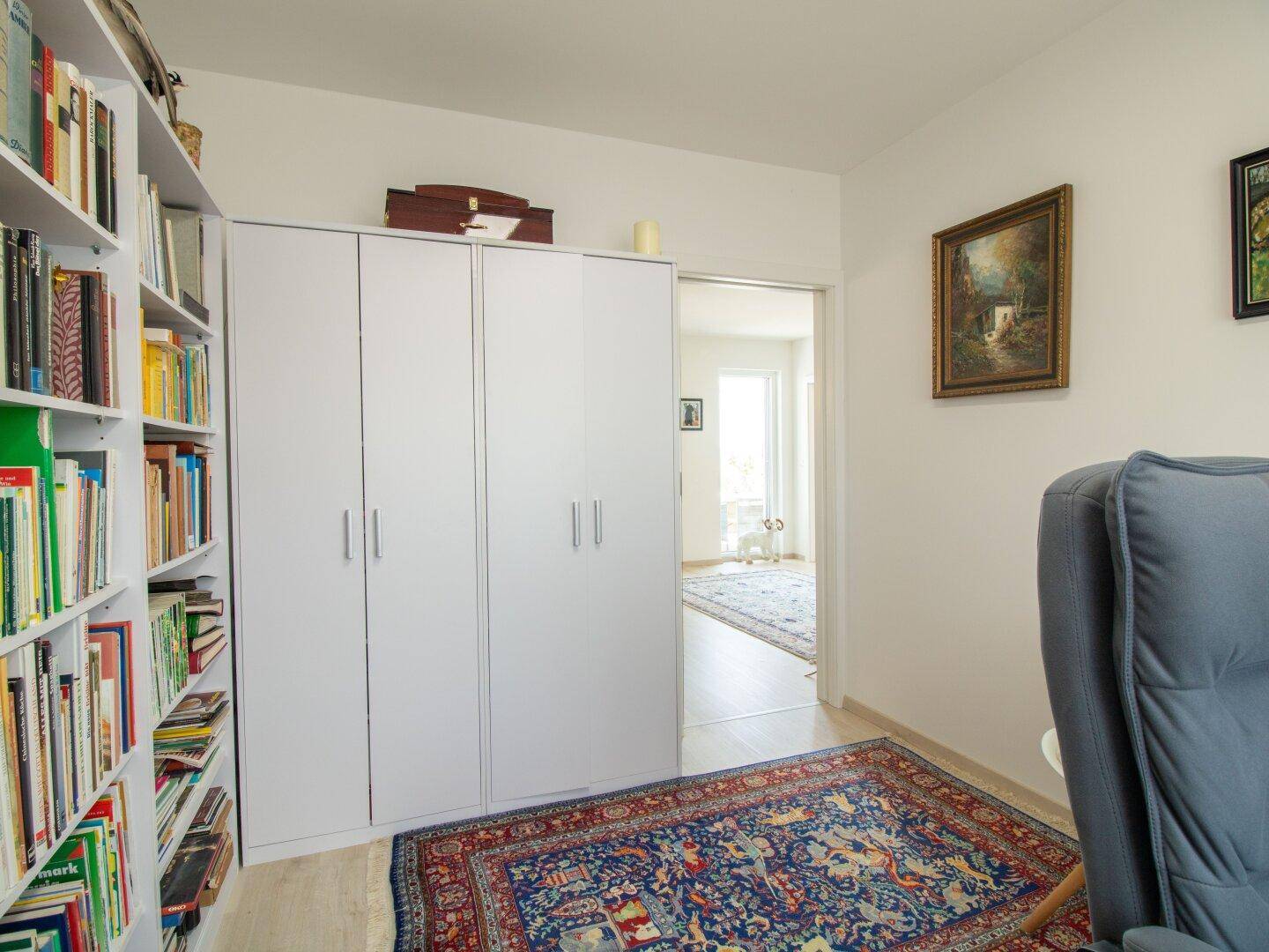 Arbeitszimmer mit Bücherregal, Kleiderschrank und Zugang zu einem weiteren Raum.