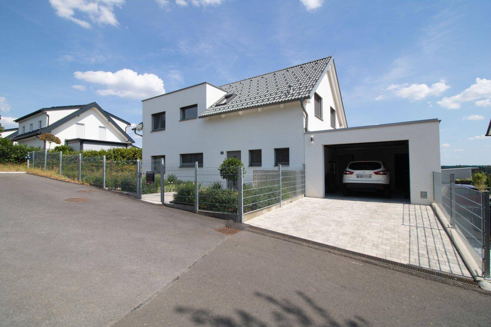 Modernes Einfamilienhaus mit Garage, gepflasterter Auffahrt und Zaun.