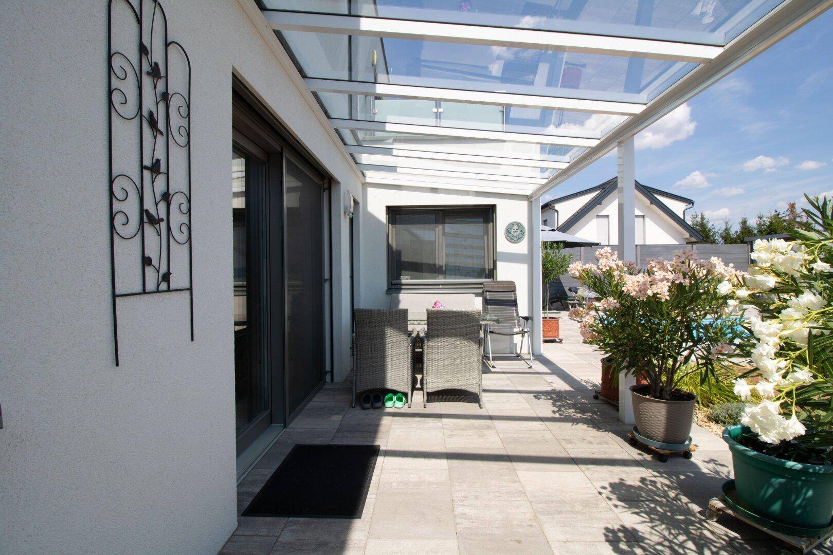 Überdachte Terrasse mit Sitzgelegenheiten und Blick auf den Garten und Pool.