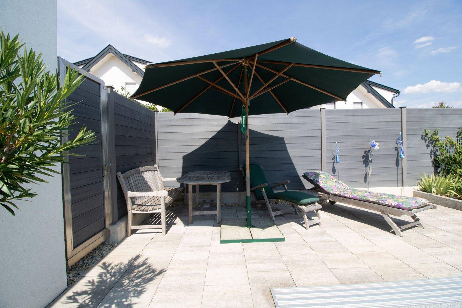 Sonniger Terrassenbereich mit Sonnenschirm, Liegestühlen und Sichtschutz.