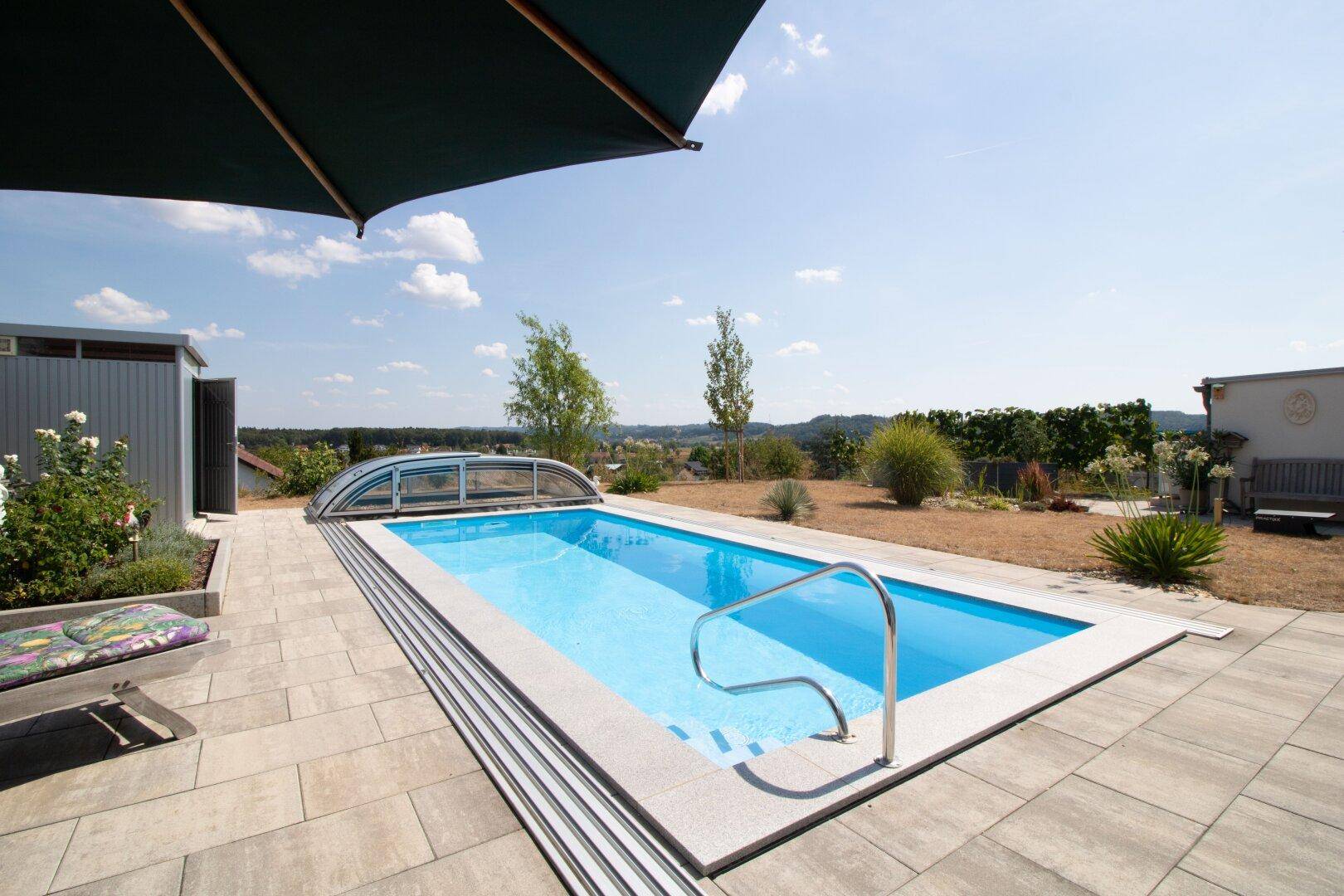 Außenpool mit Überdachung, umgeben von einer gepflasterten Terrasse und Garten.