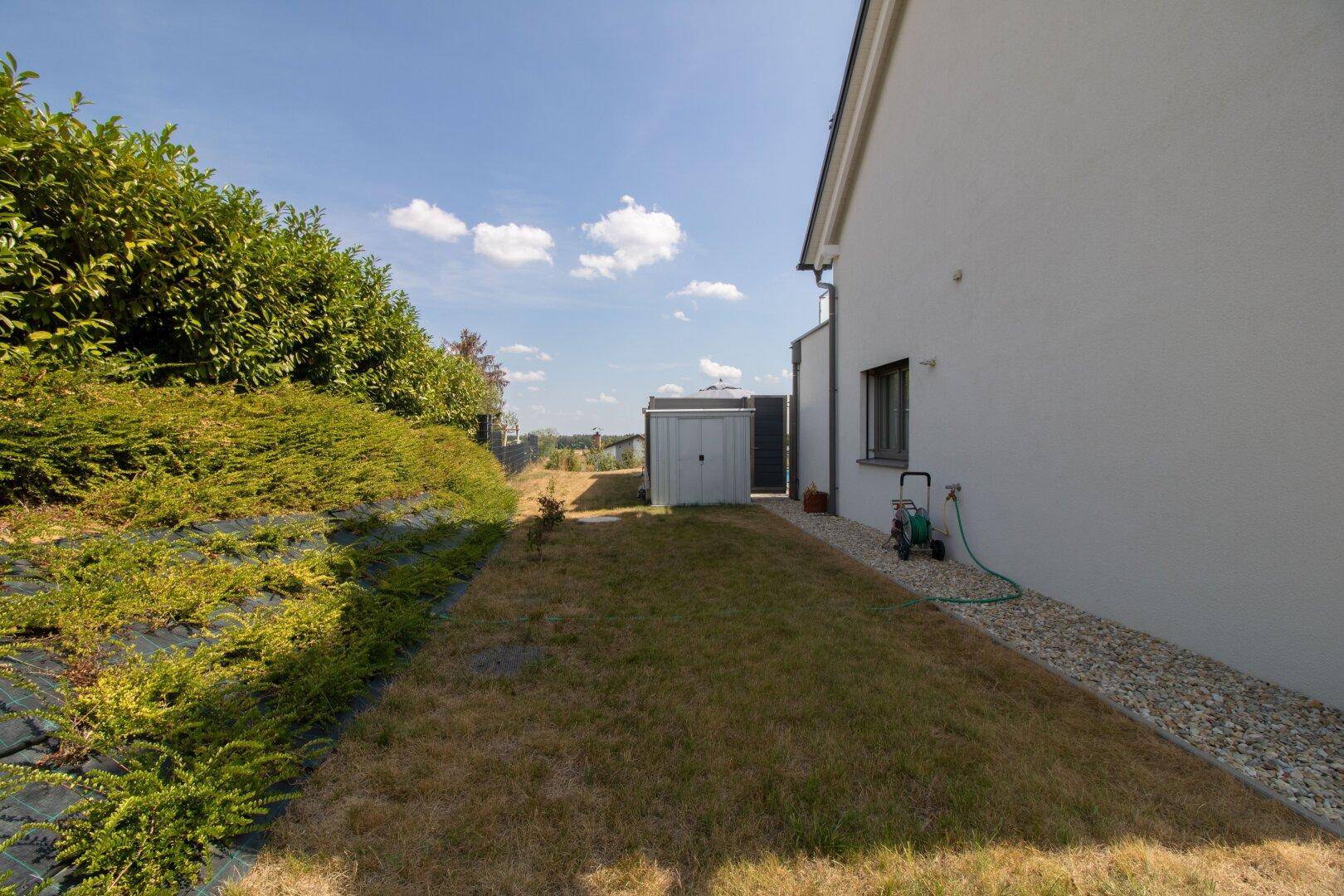 Gepflegter Gartenbereich mit Rasenfläche, Sträuchern und Gartenhaus im Hintergrund.