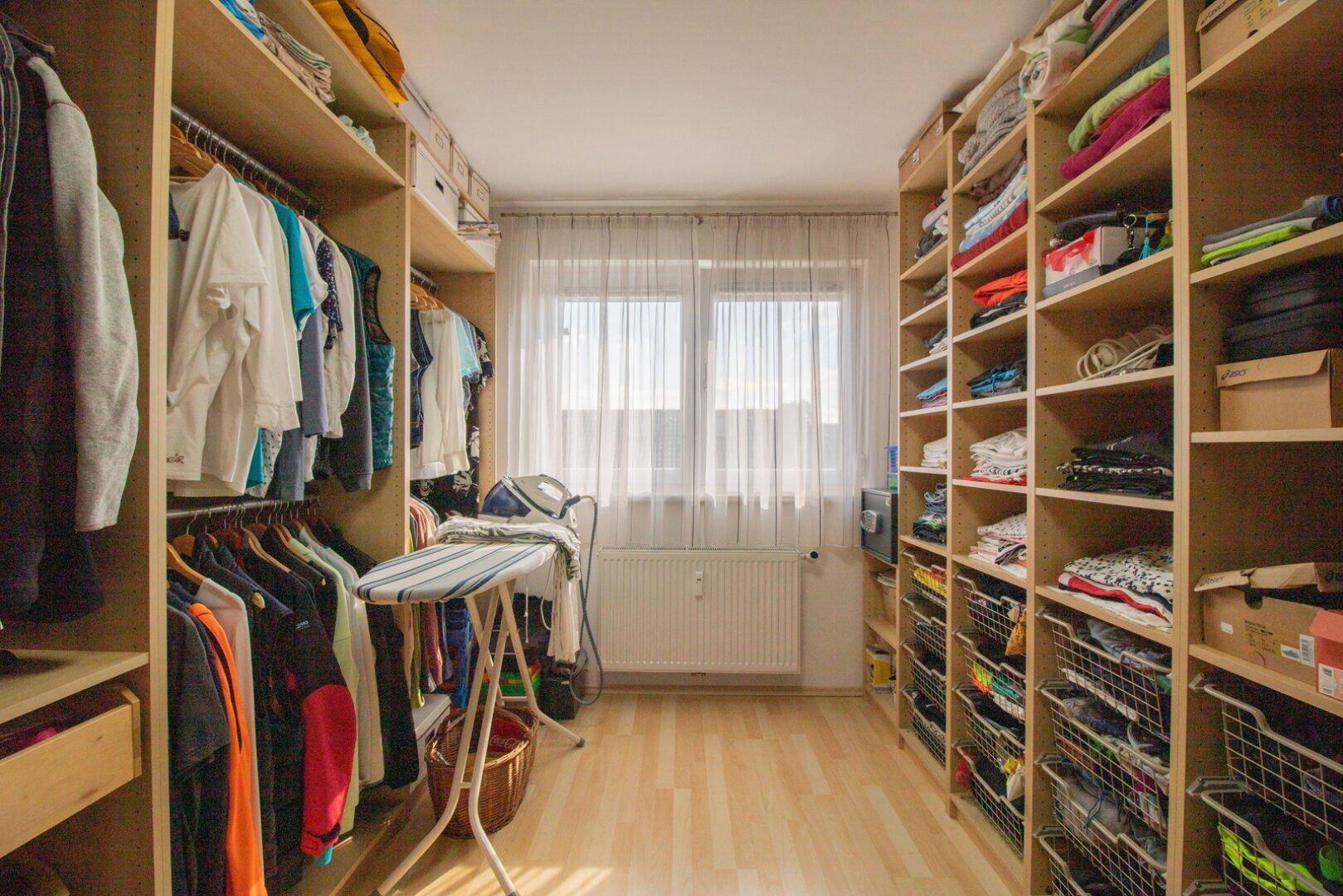 Geräumiger begehbarer Kleiderschrank mit zahlreichen Regalen und Stauraum für Kleidung und Bügelbrett.