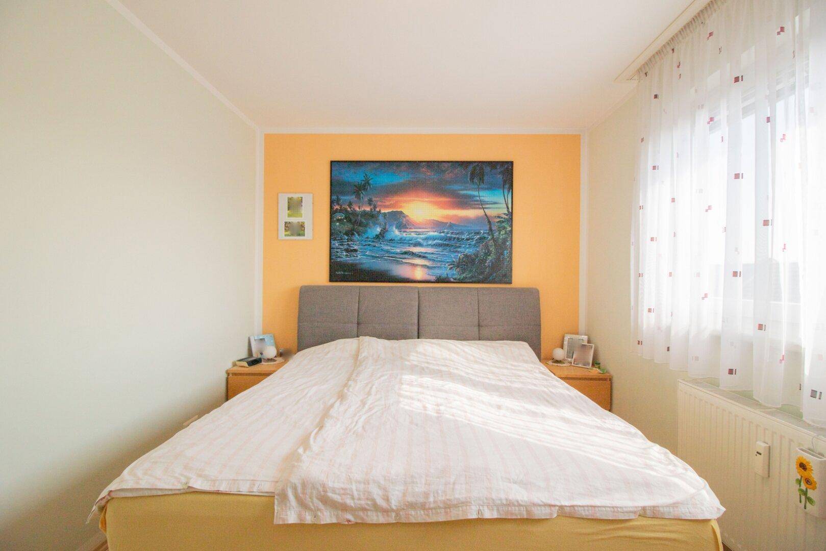 Gemütliches Schlafzimmer mit Doppelbett, Nachttischen und einem Fenster, das viel Tageslicht hereinlässt.