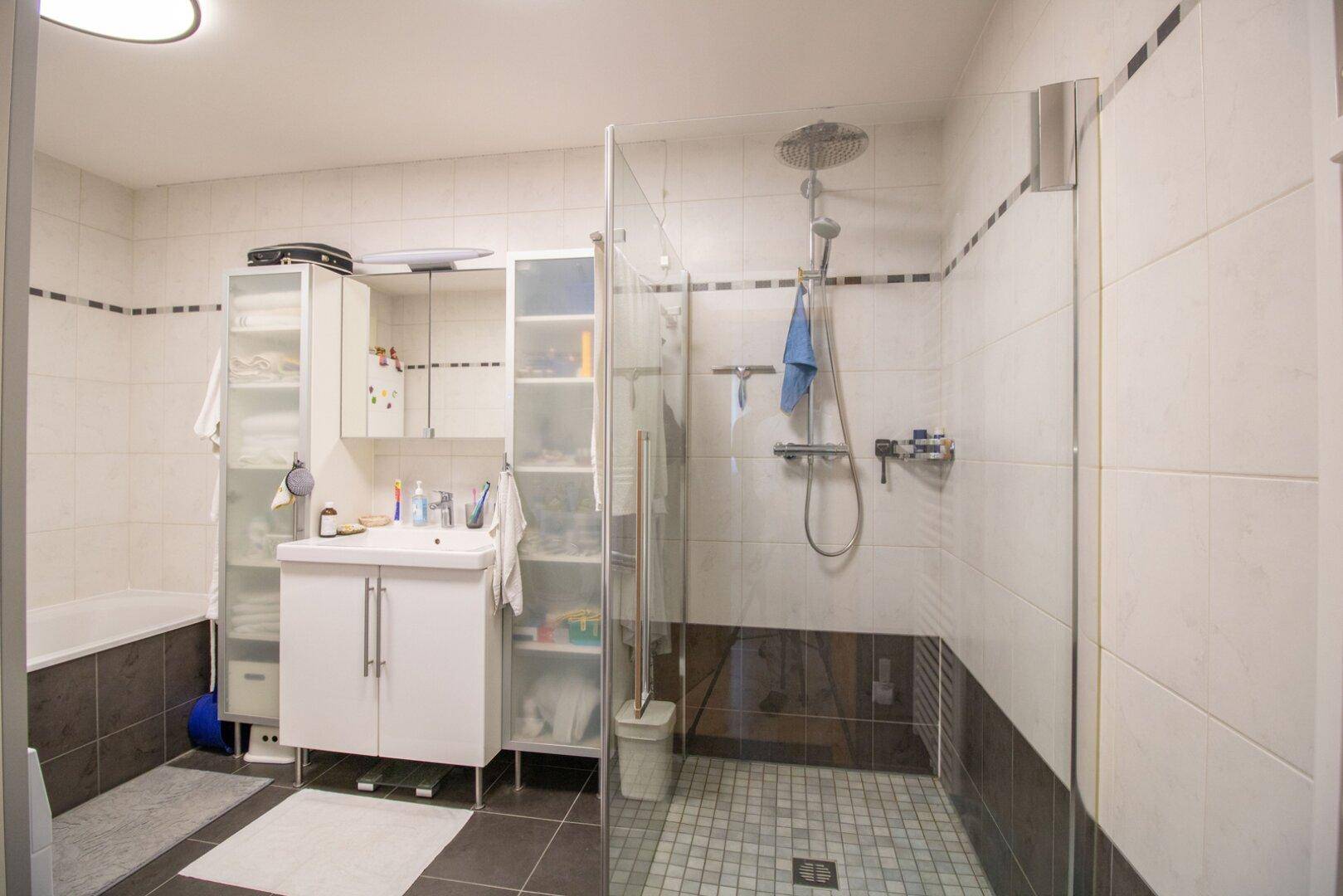 Modernes Badezimmer mit begehbarer Dusche, Badewanne und hellen Fliesen in Weiß und Anthrazit.