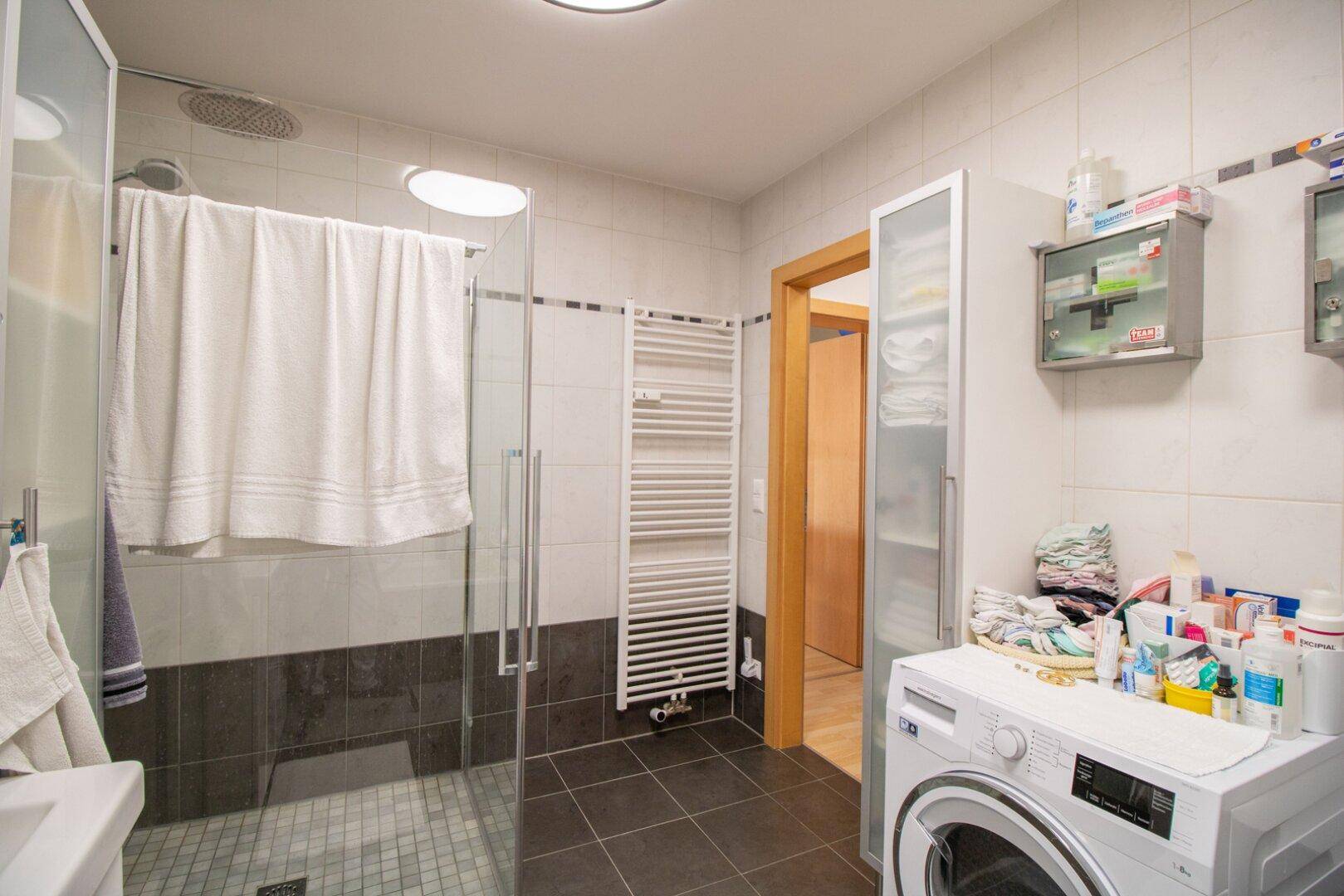 Badezimmer mit geräumiger begehbarer Dusche, beheiztem Handtuchhalter und Waschmaschine.