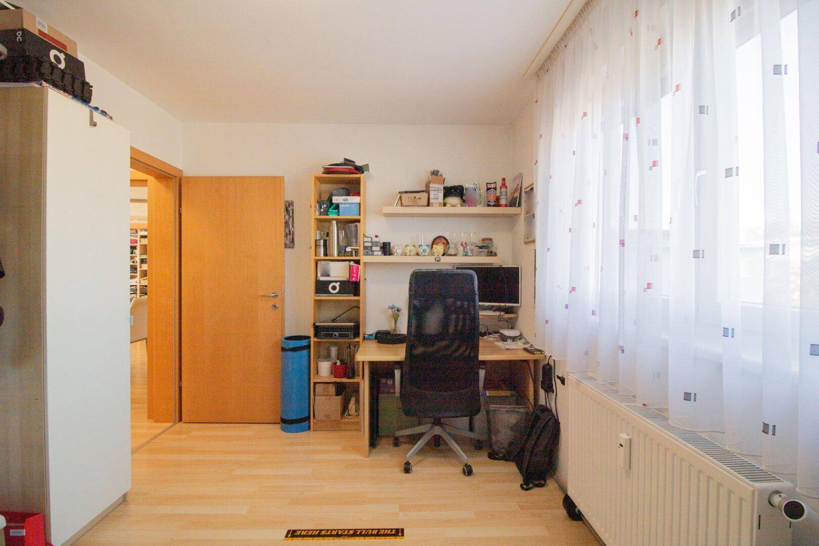 Helles Arbeitszimmer mit Schreibtisch, Regalen und einem großen Fenster, ideal für Home-Office.