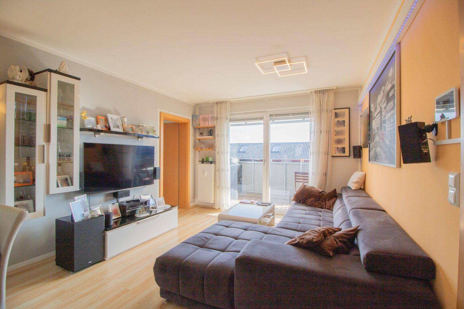 Gemütliches Wohnzimmer mit großem Ecksofa, Fernseher und direktem Zugang zum sonnigen Balkon.