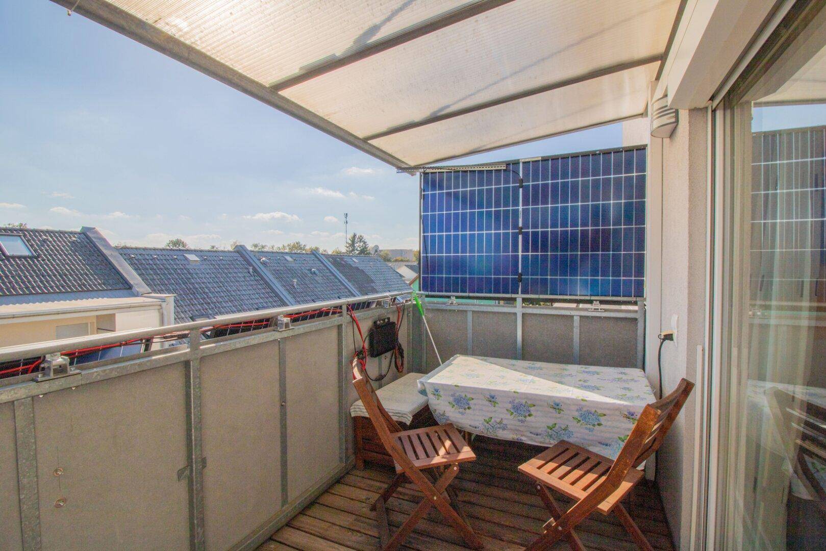 Überdachter Balkon mit Holzboden, Sitzgelegenheiten und integrierten Solarpaneelen für nachhaltige Energie.