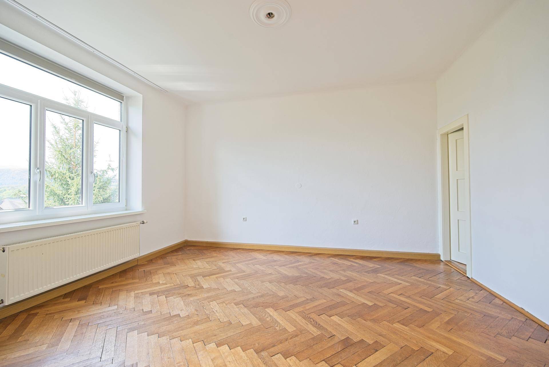 Geräumiges, helles Zimmer mit Fischgrätparkett und großen Fenstern, bereit zur individuellen Gestaltung.