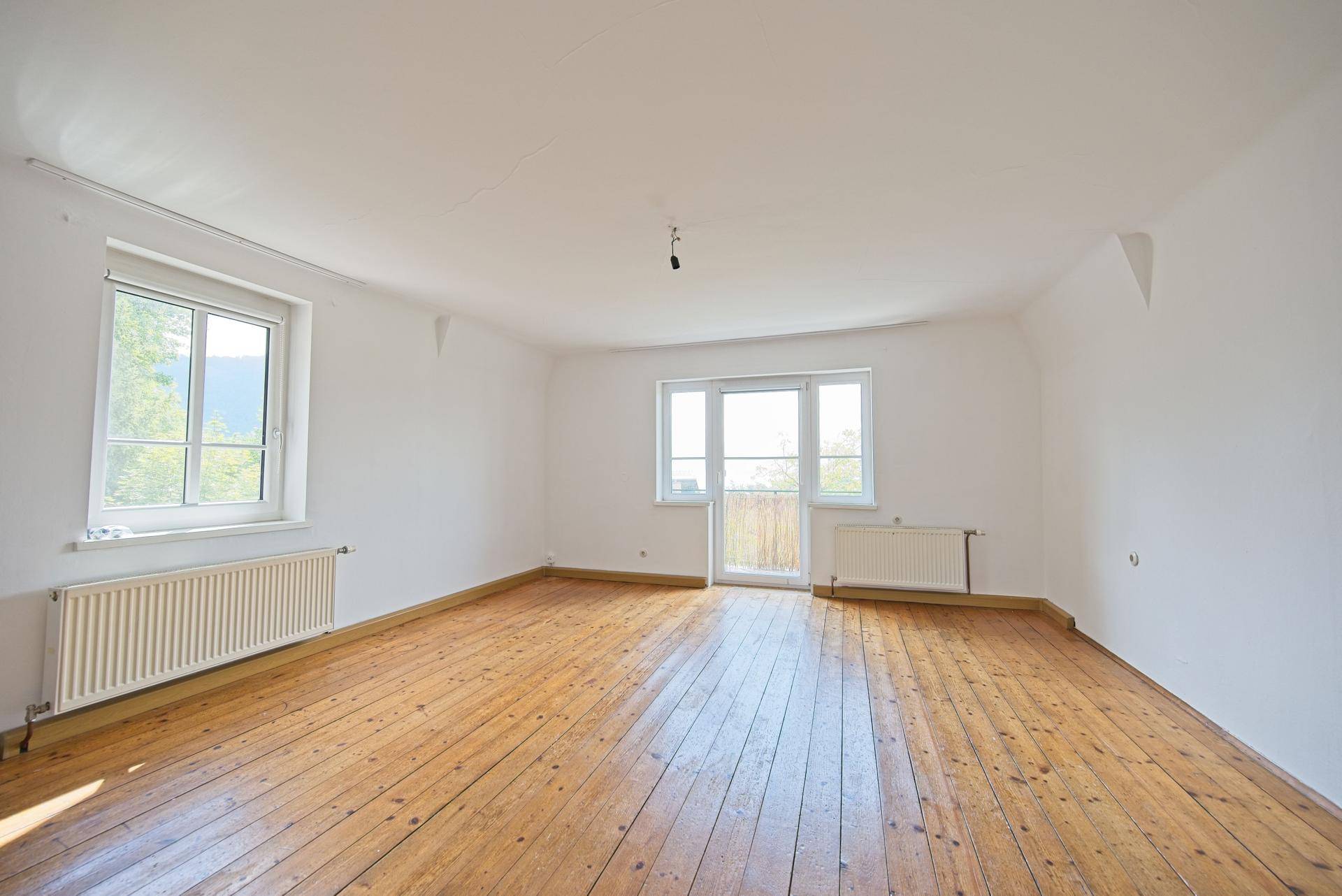 Helles, geräumiges Zimmer mit Dielenboden und großen Fenstern, die viel Tageslicht hereinlassen.